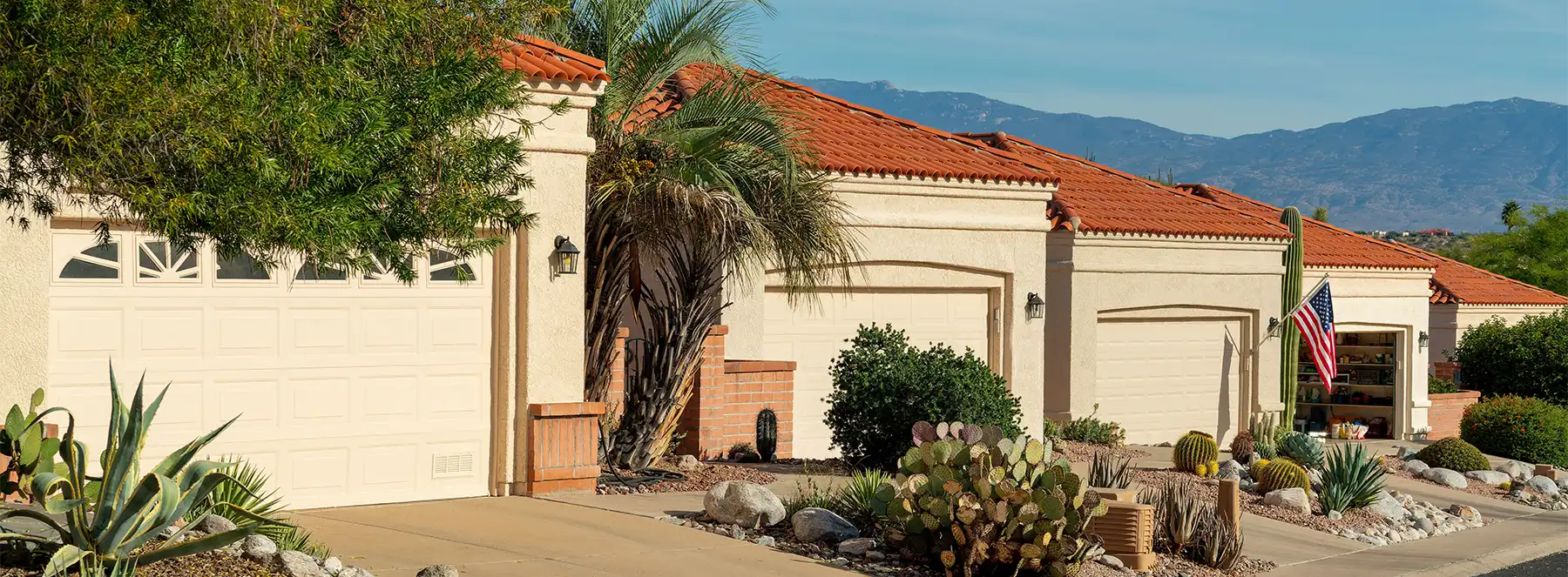 Row of beige stucco houses with red tile roofs, desert landscaping, and an American flag on one garage. trusted restoration company in Tucson