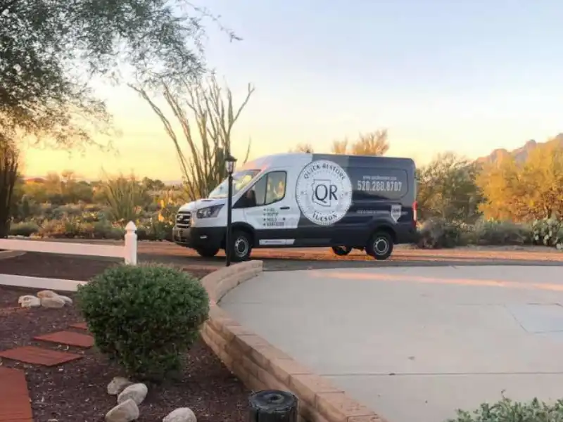 A black and white service van parked on a driveway at sunset with desert vegetation in the background. trusted restoration company in Tucson