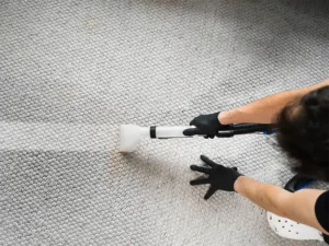 Person wearing black gloves cleaning a textured carpet with a vacuum extractor. water extraction services