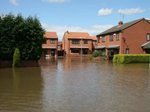 Floodwaters surround multiple brick houses in a residential neighborhood under a partly cloudy sky. flood damage repair