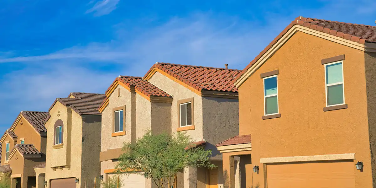 Row of suburban houses with tiled roofs under a blue sky.