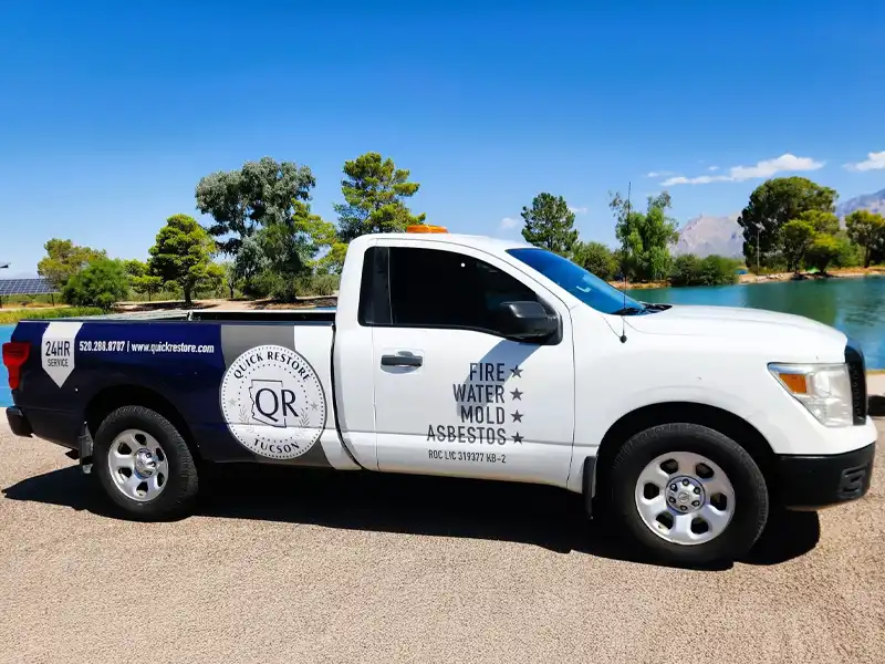 White and blue Quick Restore service pickup truck parked near a lake with trees in the background.