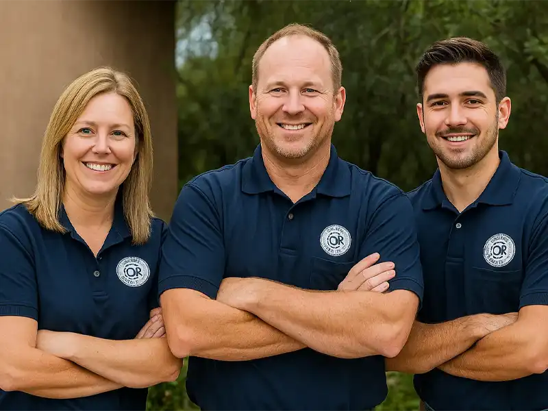 Three people in navy blue polo shirts with logos stand outdoors, smiling with arms crossed. trusted restoration company in Tucson