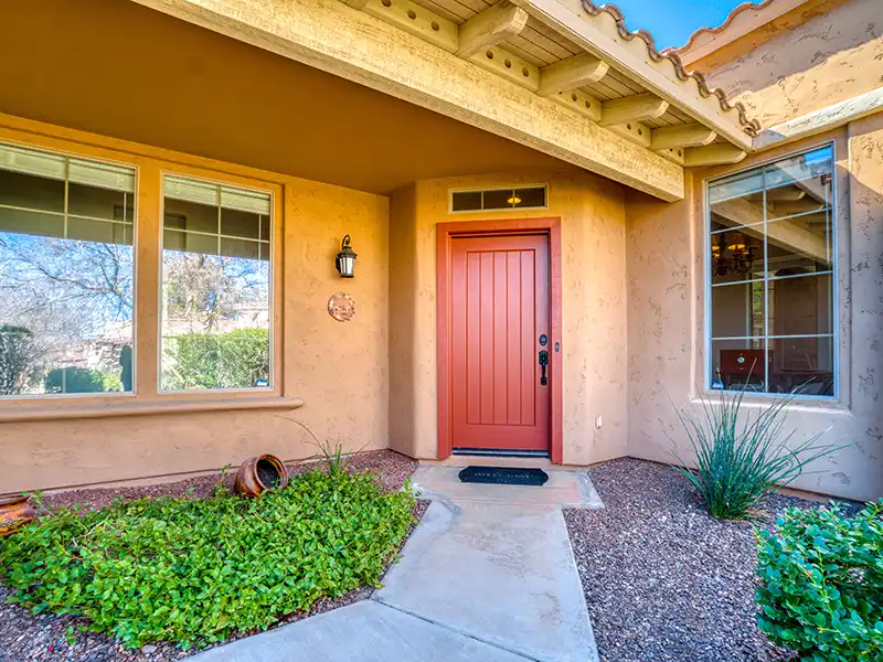 Front entrance of a house with a red door, two large windows, and surrounding greenery. water damage restoration in Tucson