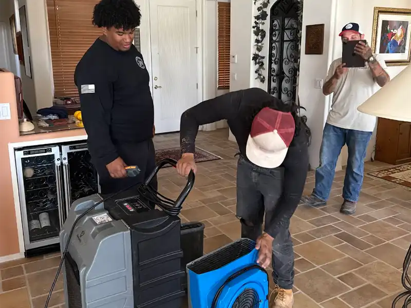 Two men operate floor drying equipment while a third man films them indoors. water damage restoration